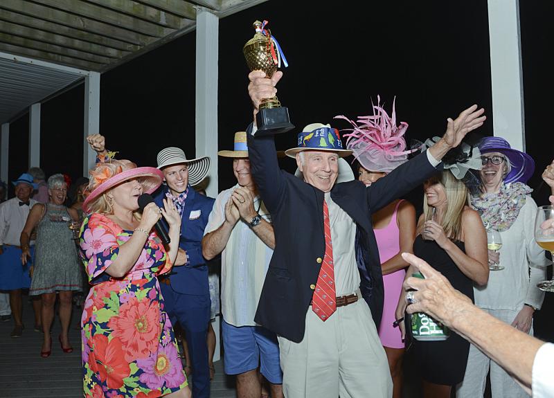 Event Chair Karen Falk announces that Albert Didden takes the cup for his inventive derby hat.